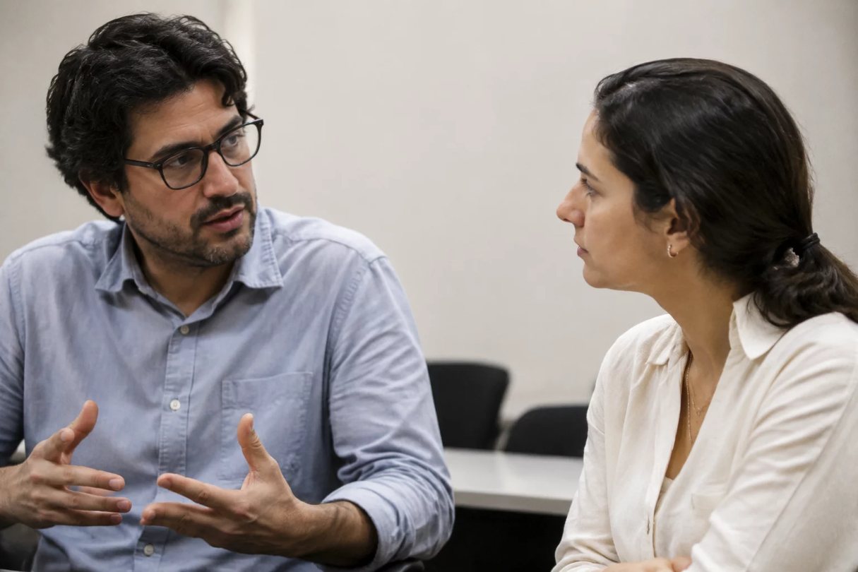 Duas pessoas frente a frente na mesa: uma sustenta a fala, a outra anota o que ouviu